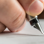 Close up of hand holding ink pen signing a document